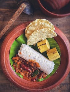 A delicious Sri Lankan breakfast featuring puttu, curry, banana, and poppadoms on a banana leaf.