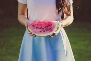 A young woman holding a juicy watermelon slice in a sunny outdoor setting.