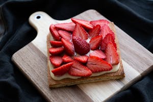 Delicious strawberry tart with cream on a wooden board, perfect for food photography.