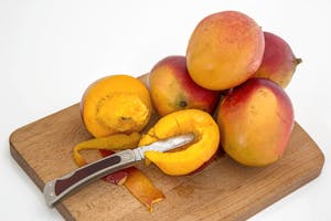 Sliced and whole mangoes on a wooden board with a knife, showcasing vibrant fruit freshness.